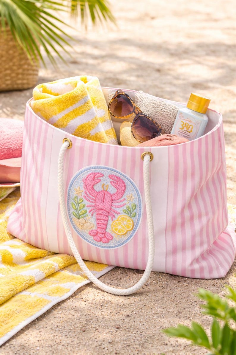 May include: Pink and white striped beach tote bag with a lobster patch. The bag is filled with a yellow and white striped towel, sunglasses, and sunscreen. The bag has white rope handles.