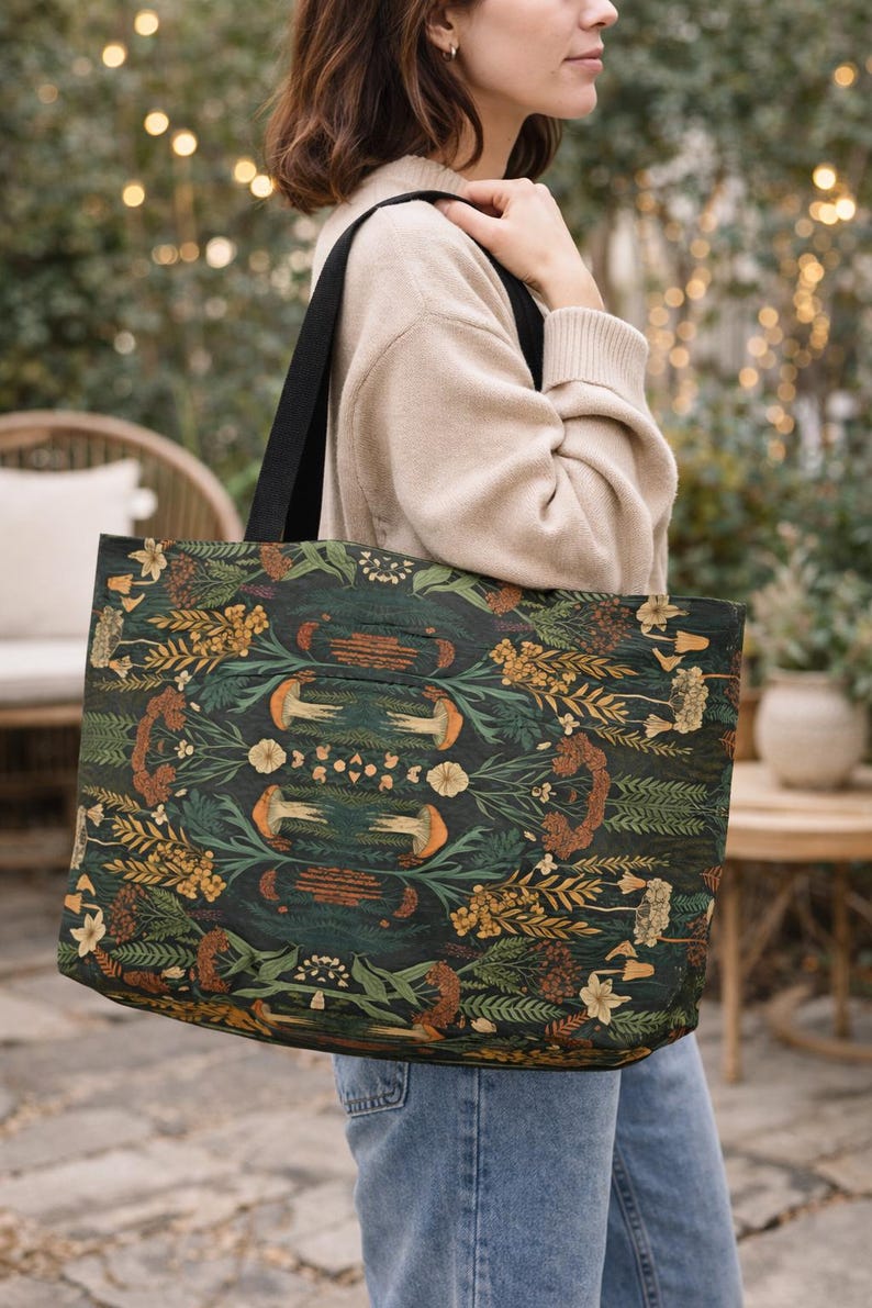 Woman wearing large dark green botanical tote bag, moody cottagecore style weekender bag with earthy nature print, everyday carryall purse