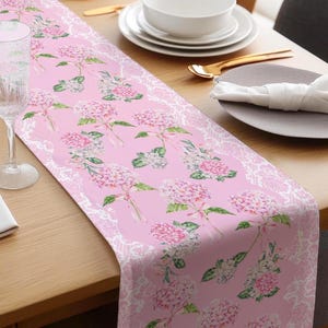 May include: A pink table runner with a white lace border and a floral pattern of pink hydrangeas.
