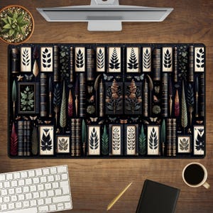 May include: A black desk mat featuring a repeating pattern of vintage books, botanical illustrations, and feathers. The design includes shades of green, brown, and gold. A keyboard, pen, notebook, and coffee cup are visible on a wooden desk.