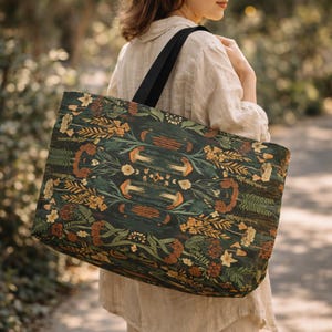 Large moody botanical tote bag carried by woman outdoors, dark green cottagecore weekender bag with nature-inspired pattern, aesthetic everyday travel tote