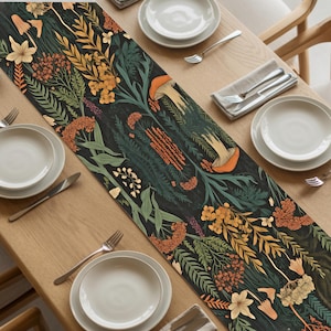 May include: A dark table runner with a botanical design featuring mushrooms, flowers, and foliage in shades of green, orange, and yellow. The runner is placed on a wooden table, with plates, silverware, and napkins visible.