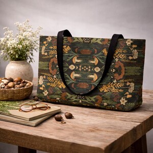 Large botanical tote bag on rustic wooden table, dark green nature pattern carryall with black straps, cottagecore travel bag styled with neutral decor