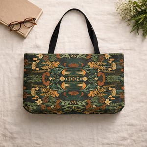 May include: A tote bag with a dark green background and a symmetrical floral pattern in shades of orange, yellow, and green. The bag has black handles and is made of a sturdy fabric. The bag is designed for carrying items.