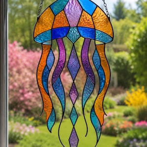 May include: A stained glass jellyfish suncatcher featuring a bell composed of orange, blue, and purple textured glass panels. The jellyfish has long, flowing tentacles made of orange, blue, and purple glass segments, all held together by black metal cames.