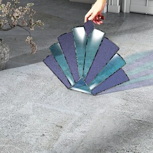 Könnte beinhalten: Ein blaues und violettes Buntglas-Sonnenstrahlen-Design mit geometrischem Muster. Der Sonnenstrahlen liegt auf einer hellgrauen Betonfläche.
