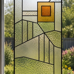 May include: A rectangular stained glass panel featuring a geometric landscape design with clear, textured glass segments in shades of light green and a central square sun motif in vibrant orange and yellow, all encased in a thin black metal frame.