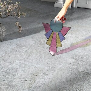 May include: A stained glass sunburst design with pink, purple, and yellow accents. The sunburst is made of glass and has a round center with a blue tint.