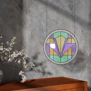May include: A round stained glass window hanging on a gray wall. The window features a geometric design with purple, yellow, and green glass pieces.