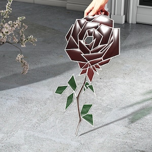 Könnte beinhalten: Eine geometrische, dunkelrote Rose mit grünen Blättern und einem Stiel. Die Rose ist in einem stilisierten, abstrakten Stil gezeichnet.