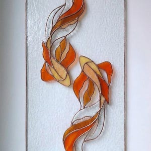 Puede incluir: Obra de arte en vidriera que representa dos carpas koi en tonos naranja, amarillo y blanco. Los peces están sobre un fondo blanco texturizado, enmarcados con un borde de cobre. Una pieza decorativa para la decoración del hogar.