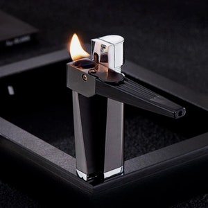 May include: A black and silver lighter with a flame coming out of the top. The lighter has a long, thin nozzle and a rectangular body.