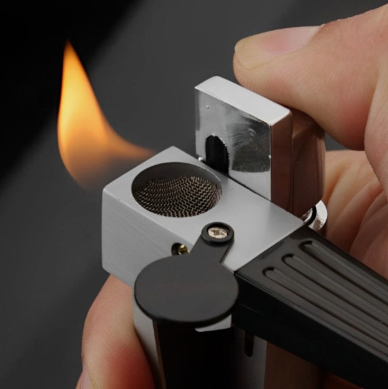 May include: A silver and black lighter with a built-in cigar cutter. The lighter is lit and the flame is visible. The lighter has a black handle and a silver body.