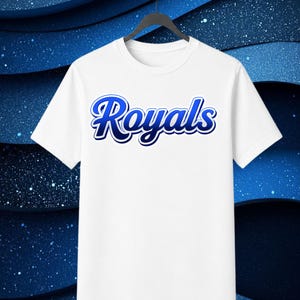 May include: A white short-sleeved t-shirt featuring the word Royals printed in a blue gradient script font across the chest. The text has a dark blue outline and a white border, creating a bold, layered effect on the plain white fabric.