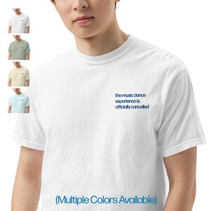 May include: A white t-shirt with the text "the music dance experience is officially cancelled" in blue lettering. The t-shirt is available in multiple colors.