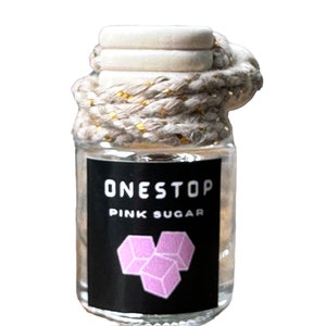 Può includere: Una piccola bottiglia di vetro con un tappo di sughero bianco e una corda dorata e bianca legata attorno alla parte superiore. La bottiglia contiene un liquido trasparente e ha un'etichetta nera con il testo "ONESTOP PINK SUGAR" e un'immagine di un cubetto di zucchero rosa.