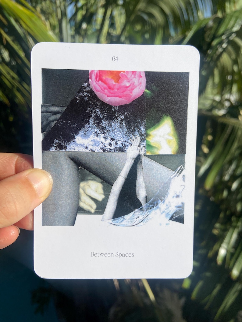 May include: A white card with the number 64 at the top and the words "Between Spaces" at the bottom. The card features a collage with a pink flower, grayscale images of body parts, and abstract shapes. The card is held by a hand.