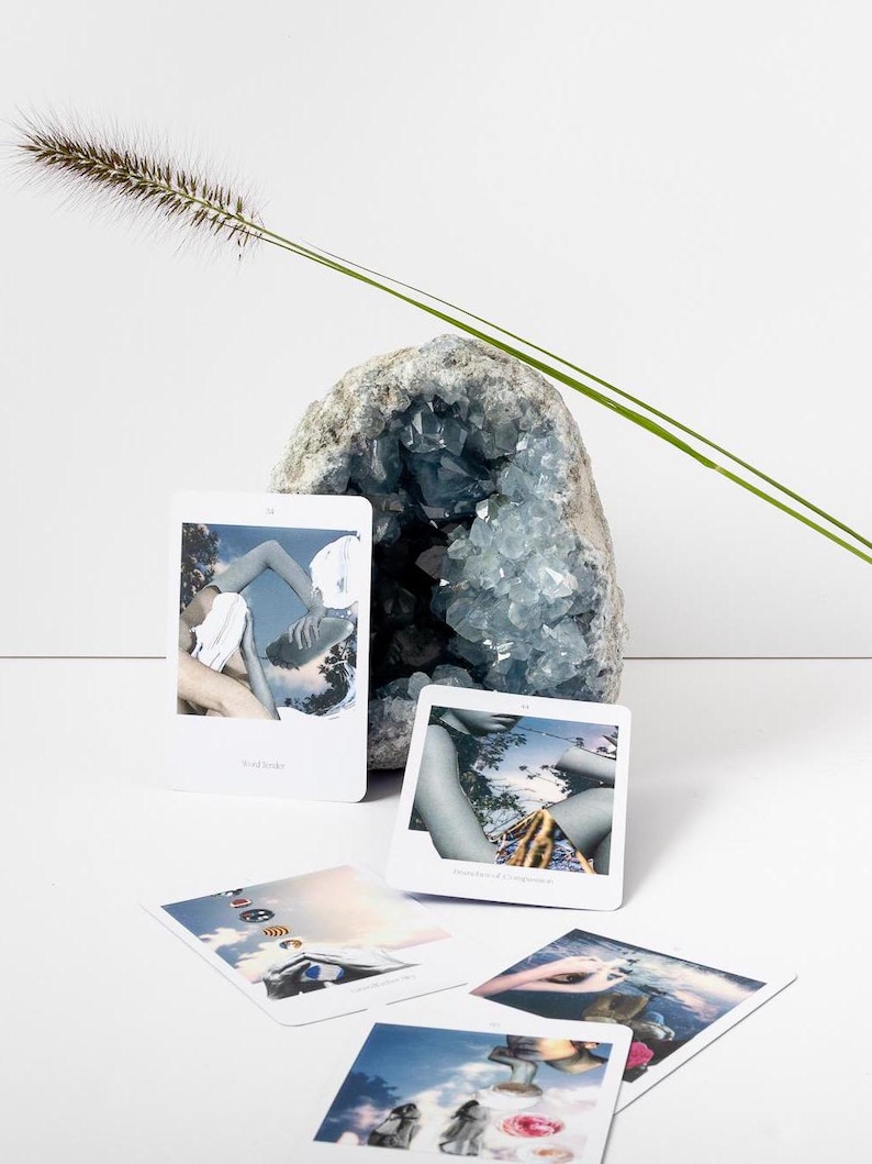 May include: A blue geode crystal formation with several small, white rectangular cards featuring images. A tall, thin green plant stem and a fluffy brown plant head are also present. The cards have text.