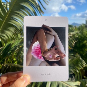 May include: A rectangular card with the number 28 at the top features a black and white image of a person's arms and legs, a pink flower, and a hand with a gold bracelet. The text "Temple Body" is at the bottom of the card.