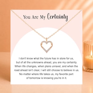 May include: A rose gold-tone heart pendant necklace on a delicate chain, displayed on a card featuring the text 'You Are My Certainty' and a printed message about the future, set against a light pink background with a white arch design.
