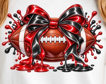 Pode incluir: Uma t-shirt branca de manga curta com uma impressão gráfica de uma bola de futebol americano castanha adornada com um grande laço brilhante vermelho e preto, rodeada por salpicos de tinta vermelha e preta vibrantes.