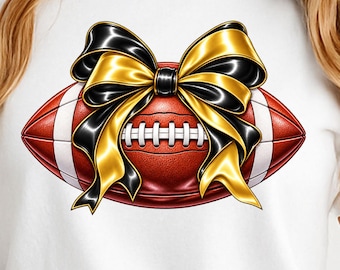 Pode incluir: Uma t-shirt branca de manga curta com uma impressão gráfica de uma bola de futebol americano castanha adornada com um grande laço brilhante preto e dourado. O design está centrado no peito e apresenta uma textura realista.