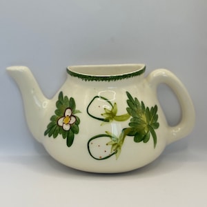 Puede incluir: Tetera de cerámica blanca con un diseño pintado a mano de fresas y hojas en verde y marrón. La tetera tiene un pico y una asa.