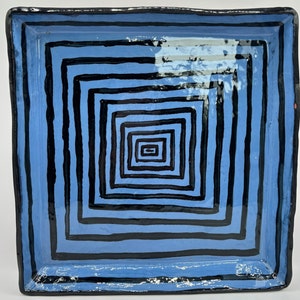 May include: A blue ceramic square tray with a black and white geometric pattern. The pattern is made up of concentric squares that get smaller as they go towards the center of the tray.