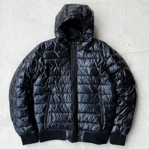 May include: A black hooded puffer jacket with a shiny finish. The jacket has a zipper closure and two zippered pockets.