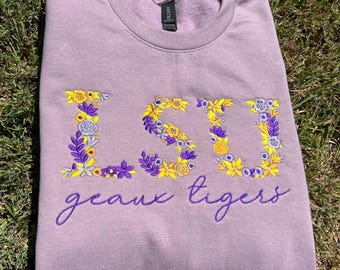 May include: Purple sweatshirt with a floral embroidered LSU logo and the text "geaux tigers" in purple.