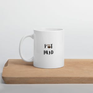 May include: White ceramic coffee mug with a black graphic of a coffee pot and the text "POT HEAD".