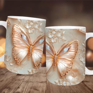 May include: Two white ceramic mugs with a butterfly design. The butterfly has gold-colored wings with a pearl-like sheen and is set against a cream-colored background with floral accents. The mugs have white handles.