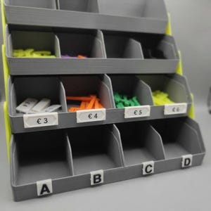May include: A gray tiered storage rack with bright yellow side supports, featuring multiple open compartments. The middle row has white labels marked &euro;3, &euro;4, &euro;5, and &euro;6, while the bottom row has white labels marked A, B, C, and D.