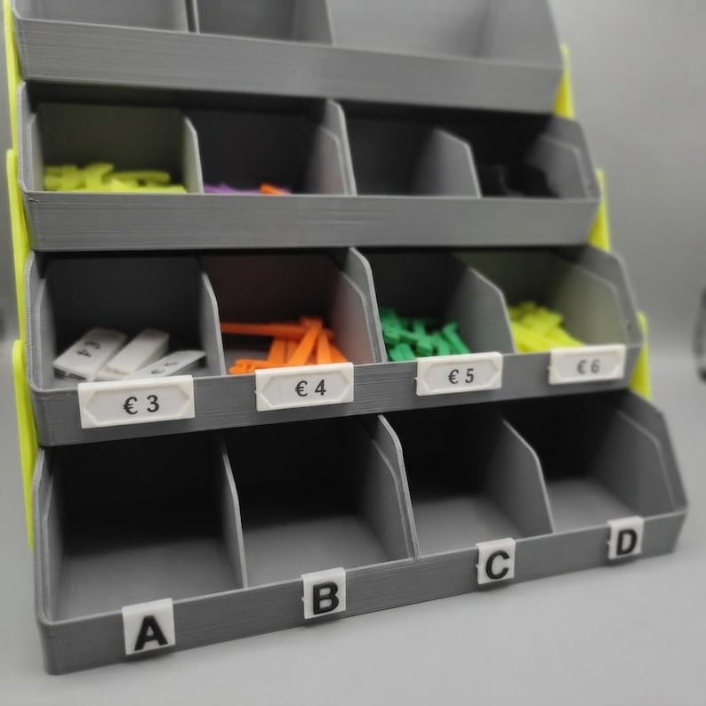 May include: A gray tiered storage rack with bright yellow side supports, featuring multiple open compartments. The middle row has white labels marked &euro;3, &euro;4, &euro;5, and &euro;6, while the bottom row has white labels marked A, B, C, and D.