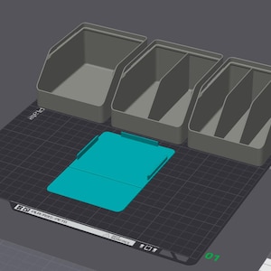 May include: A digital 3D rendering of three grey storage bins with varying internal compartment configurations and one flat, rectangular teal-colored base plate, all arranged on a dark grey grid surface with visible software interface icons.