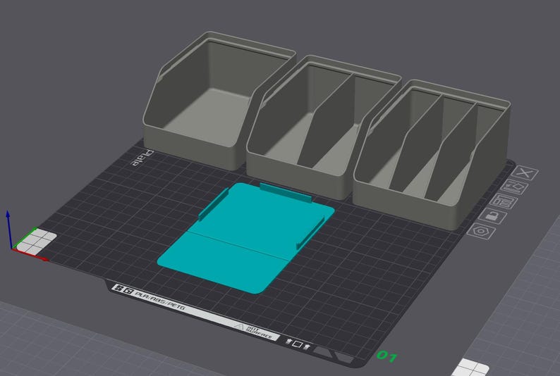 May include: A digital 3D rendering of three grey storage bins with varying internal compartment configurations and one flat, rectangular teal-colored base plate, all arranged on a dark grey grid surface with visible software interface icons.