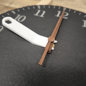 May include: Close-up of a black slate clock face with white numerals and a white hour hand. The minute and second hands are made of brown wood. The clock hands point to approximately 11:59.
