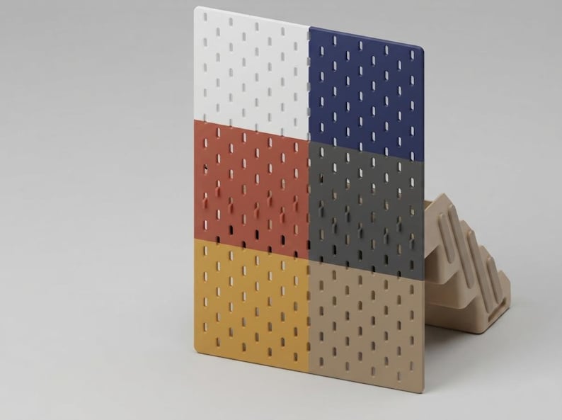 May include: A rectangular pegboard panel featuring a grid of vertical slots, divided into six distinct color sections: white, dark blue, terracotta, dark gray, mustard yellow, and beige, supported by a beige plastic stand on the right side.