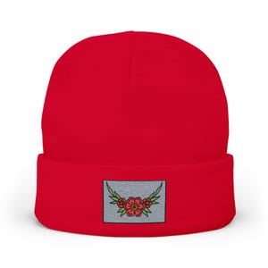 Peut inclure: Un bonnet en tricot rouge vif doté d'un écusson rectangulaire sur le revers avant. L'écusson est gris clair et présente un motif brodé composé d'une fleur rouge centrale avec des feuilles vertes s'étendant de chaque côté de manière symétrique.