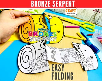 Può includere: Un'attività di bricolage in carta con un'illustrazione gialla, blu e arancione di un serpente con il testo Bronze Serpent Number 21. Sotto, una versione in bianco e nero dello stesso disegno si apre per rivelare un libretto con testo e disegni.