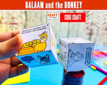 May include: Two paper cube crafts featuring the story of Balaam and the donkey. One cube is coloured with illustrations of a yellow donkey and blue speech bubbles, while the other is a black and white outline version for colouring.