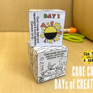 Pode incluir: Dois cubos brancos, um empilhado sobre o outro, com ilustrações coloridas e texto. O cubo superior diz "DIA 1" com um gráfico de sol e o texto "Deus fez a luz e separou-a das trevas". O cubo inferior diz "DIA 3" com um desenho de plantas e árvores.