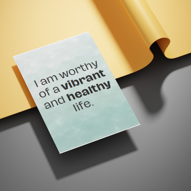 May include: A white card with the text "I am worthy of a vibrant and healthy life" in black font. The card is set against a yellow and gray background, with a rolled-up section of the yellow paper visible.