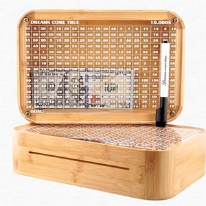 May include: A wooden savings box with a clear acrylic top, featuring a grid for tracking savings goals up to $10,000. The box includes a dry-erase marker and the words "DREAMS COME TRUE".
