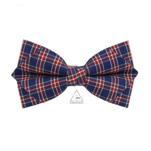 Op de afbeelding: Een blauwe geruite vlinderdas met rode en witte accenten. Deze klassieke accessoire is perfect voor formele evenementen of om een vleugje stijl aan elke outfit toe te voegen. De vlinderdas heeft een symmetrisch ontwerp en is gemaakt van geweven stof.