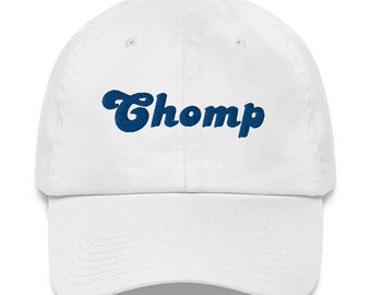 Könnte beinhalten: Weiße Baseballkappe mit einem blauen gestickten Logo, auf dem in einer Retro-Schrift "Chomp" steht.