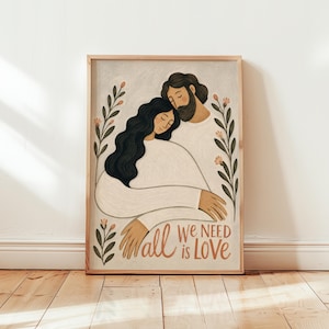 May include: A framed art print featuring an illustration of two figures embracing, one with long dark hair and one with a beard, both wearing white clothing. The artwork is framed in light wood and includes the text all we need is love.