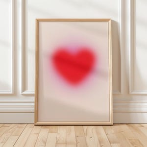 May include: A framed print featuring a blurred red heart shape against a pale pink background.