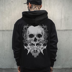 May include: Black hooded sweatshirt featuring a large white skull graphic on the back. The skull design includes intricate details and the word "SINNER" in a stylized font. The sweatshirt has a drawstring hood.
