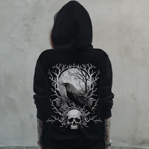 May include: Black hooded sweatshirt featuring a detailed graphic on the back. The design includes a raven, bare trees, and a skull, all in shades of gray and white. The sweatshirt is a dark color and has a hood.